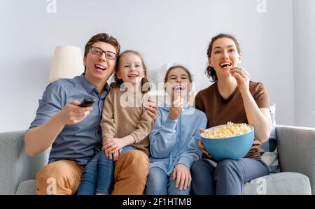 Bonne famille regardant la télévision avec pop-corn à la maison. Mère, père et filles passent du temps ensemble. Banque D'Images