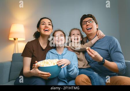 Bonne famille regardant la télévision avec pop-corn à la maison. Mère, père et filles passent du temps ensemble. Banque D'Images