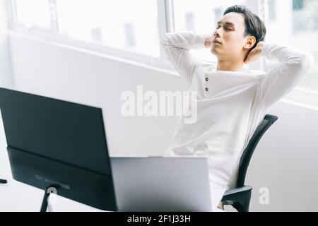 Le programmeur asiatique est assis avec sa tête dans sa chaise pour se détendre après un temps de travail fatigant Banque D'Images