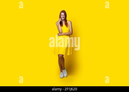 Photo monochrome d'une femme caucasienne avec des cheveux rouges une robe jaune souriant à la caméra sur le mur du studio Banque D'Images