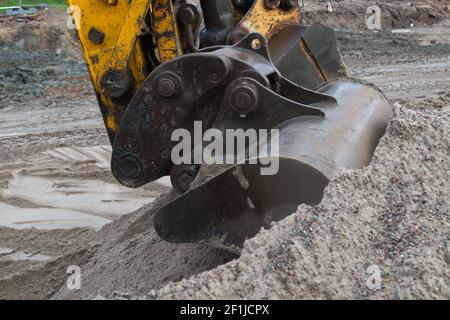 Le godet en métal de fer d'une grande pelle hydraulique jaune creuse une pile de terre sur un chantier de construction dans le processus de révision de la route, contre le dos Banque D'Images