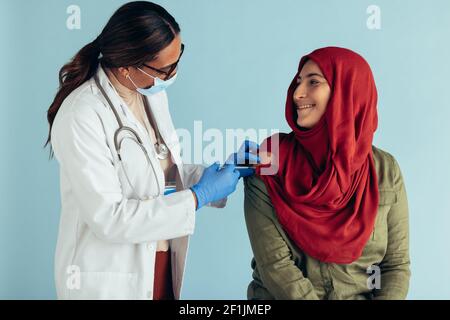 Médecin portant un masque facial et des gants de protection donnant une dose de vaccin à la femme en hijab. Femelle musulmane du hijab recevant la vaccination. Banque D'Images