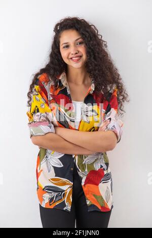 UN ADOLESCENT HEUREUX AUX CHEVEUX BOUCLÉS REGARDANT L'APPAREIL PHOTO AVEC LES BRAS FERMÉ Banque D'Images