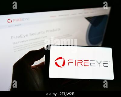 Personne portant un smartphone portant le logo de la société de cybersécurité américaine FireEye Inc. À l'écran devant le site Web. Mise au point sur l'affichage du téléphone. Photo non modifiée. Banque D'Images