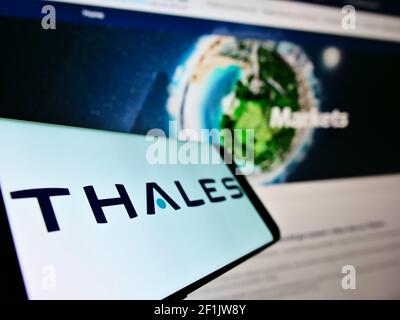 Smartphone avec logo de la société française de défense Thales S.A. sur écran en face de la page web des affaires. Mise au point au centre-gauche de l'écran du téléphone. Banque D'Images