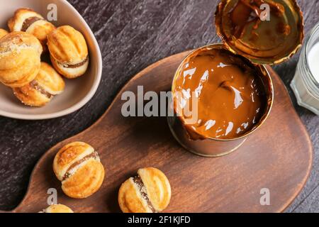 Biscuits savoureux et boîte de lait concentré bouilli arrière-plan sombre Banque D'Images