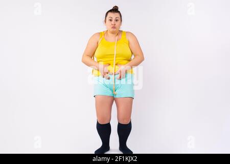 Perte de poids, amincissement, concept de régime. Plus taille, femme XXL dans les vêtements de maison avec mètre ruban autour de la taille, montrant l'abdomen gras avec drôle Banque D'Images