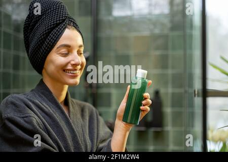 Femme après la douche tenant une bouteille avec shampooing vert dans la salle de bains. Concept beauté et soin. Produits de soins capillaires. Banque D'Images