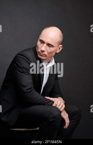 Portrait d'un entrepreneur sérieux et pensif d'âge moyen et chauve assis sur une chaise et regarder loin Banque D'Images