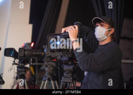 un caméraman masqué filme un spectacle télévisuel en studio. TÉLÉVISION Banque D'Images