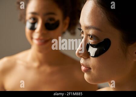 Portrait rapproché de deux jeunes femmes de race mixte posant avec des taches noires appliquées sous les yeux. Concept de soins de beauté. Mise au point sélective Banque D'Images