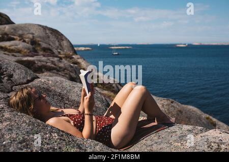 Femme lisant un livre sur la côte rocheuse Banque D'Images