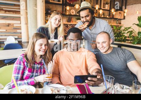 Une compagnie de jeunes multiculturels dans un café manger de la pizza, boire des cocktails, s'amuser Banque D'Images