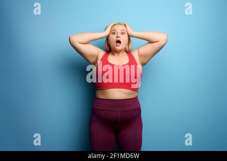 FAT girl dans la suite de fitness veut commencer un régime mais a certains. Fond cyan Banque D'Images