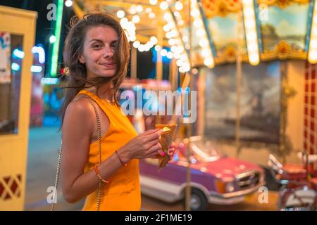 Portrait d'une jeune femme avec des cheveux soufflés sur son visage se poser heureux à côté des manèges du parc d'attractions Banque D'Images