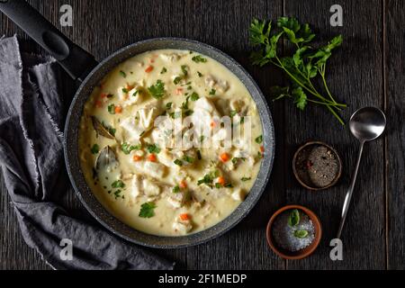poisson poché dans une sauce à base de lait avec légumes, épices et herbes dans une casserole sur une table en bois, cuisine anglaise Banque D'Images