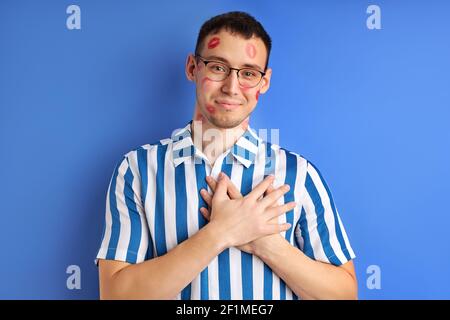 Portrait drôle de jeunes caucasiens nerd avec des empreintes de baiser isolé sur fond bleu, le gars heureux automne dans l'amour avec quelqu'un, se tenir dans la bonne humeur. Les gens Banque D'Images