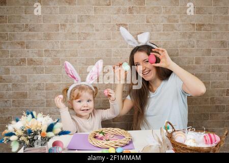 Belle jeune femme avec petite fille mignonne se préparent pour la célébration de Pâques. Maman et fille portant des oreilles de lapin s'amusent à la maison. Banque D'Images