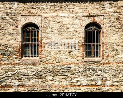 Deux fenêtres avec grilles en métal rouillé sur un mur en pierre. Texture architecturale. Façade de prison historique avec surface en brique. Construction médiévale Banque D'Images