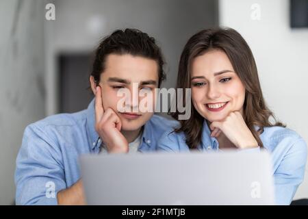 Agréable couple de famille assis à une grande table en bois dans la cuisine moderne, regardant l'écran d'ordinateur portable. Heureux jeune mixte race marié conjoint web surf, mak Banque D'Images