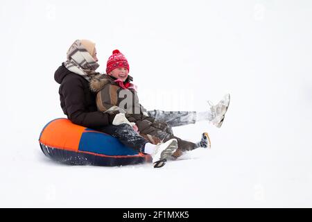 Animations en hiver. Les gens gais vêtiés de vêtements chauds descendent une montagne enneigée sur un traîneau. Banque D'Images