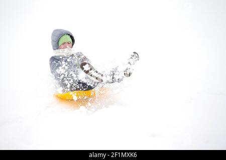 Enfant en hiver. Une petite fille gaie en vêtements chauds descend une montagne enneigée sur un traîneau. Banque D'Images