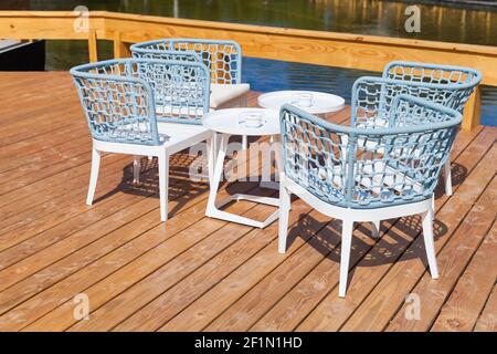 Des chaises et des tables blanches bleues sont vides sur une terrasse avec parquet par temps ensoleillé Banque D'Images