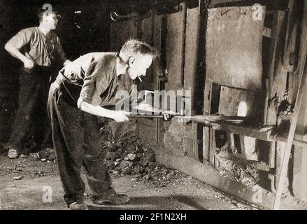 Une image vers les années 1930 d'un homme qui pudling de la fonte dans une fonderie de fer britannique. Le processus de puddling est une étape dans la fabrication de fer de haute qualité à l'aide d'un creuset ou d'un four, inventé en Grande-Bretagne pendant la Révolution industrielle. Le fer à barres pourrait être produit sans charbon de bois et a remplacé les procédés d'enrobage et d'estampage, d'utilisation du charbon de bois et de bloomerie précédents. Banque D'Images