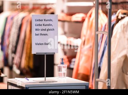 Berlin, Allemagne. 09e mars 2021. À l'entrée d'un magasin de vêtements, il y a un distributeur de désinfectant et un panneau indiquant « client de la marque, nous serons avec vous dans un instant. Merci beaucoup". Depuis 09.03.2021, les premiers clients sont de nouveau autorisés à magasiner sur rendez-vous dans les magasins de détail. Credit: Kira Hofmann/dpa-Zentralbild/dpa/Alay Live News Banque D'Images