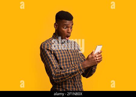 Portraif de l'homme noir drôle choqué regardant l'écran de smartphone avec la bouche ouverte, excité afro-américain gars émotionnellement réagissant au bon en ligne o Banque D'Images