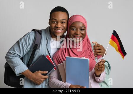 Joyeux afro-américain étudiants musulmans jeune homme et femme dans le hijab portant le drapeau allemand sur fond gris studio, portant des sacs à dos et ne tenant pas Banque D'Images