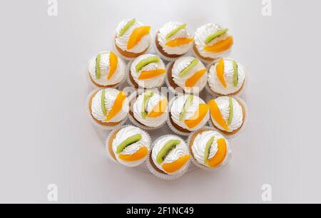 Vue de dessus des petits gâteaux frais. Crème au beurre au fromage et fruits - kiwi et pêche. Desserts sucrés sur fond gris avec un espace vide pour le texte. Style de pose à plat Banque D'Images