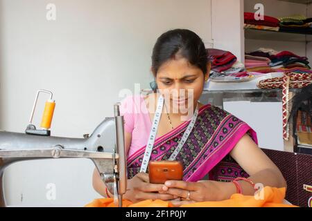 femme indienne tailleur tenant le téléphone mobile à l'atelier Banque D'Images