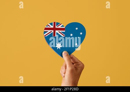 gros plan d'un homme tenant dans sa main un drapeau australien en forme de coeur, fait avec des découpes de papier de différentes couleurs, sur un backgroun jaune Banque D'Images