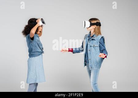 une fille afro-américaine stupéfait de regarder un ami jouer dans vr casque sur gris Banque D'Images