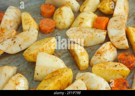 Pommes de terre et carottes crues pelées et hachées avec des épices sur une plaque à pâtisserie. Gros plan. Banque D'Images