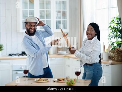 Un jeune couple noir se bat avec des ustensiles de cuisine, s'amuser à la maison. Les conjoints afro-américains gaies se visent avec Roller PIN et SP Banque D'Images