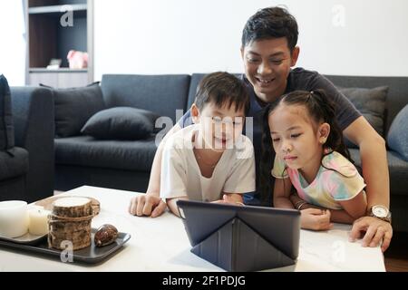 Un père souriant positif et ses deux enfants apprécient de passer du temps ensemble et regarder des programmes éducatifs sur une tablette numérique Banque D'Images