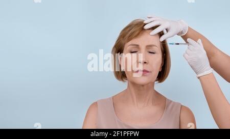 Belle femme âgée qui reçoit l'injection de beauté de la part du cosmetologiste sur fond de studio léger, bannière design avec l'espace de copie. Esthéticienne donnant anti-agin Banque D'Images