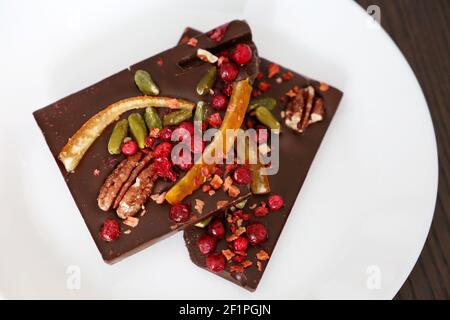 Chocolat noir avec canneberges séchées, agrumes et noix. Dessert savoureux sur une assiette blanche Banque D'Images