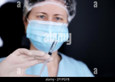Médecin avec seringue, femme dans un masque médical et gants de protection se préparant à l'injection. Concept de vaccination pendant la pandémie de Covid-19 Banque D'Images