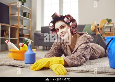 Une femme heureuse en curlers, masque de beauté et gants en caoutchouc se détendant après avoir fait tous les travaux ménagers Banque D'Images