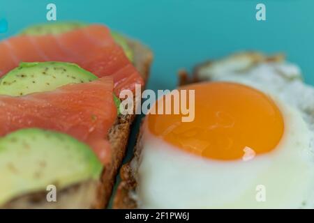 Pain grillé maison avec saumon et avocat sur une tranche de pain aux céréales. Œufs frits au jaune vif sur fond de menthe Banque D'Images