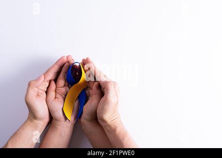 Le jour du syndrome de Down, les mains d'homme et de femme tenant le ruban bleu jaune de sensibilisation soutiennent le patient avec l'incapacité de la maladie Banque D'Images