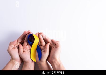 Le jour du syndrome de Down, les mains d'homme et de femme tenant le ruban bleu jaune de sensibilisation soutiennent le patient avec l'incapacité de la maladie Banque D'Images