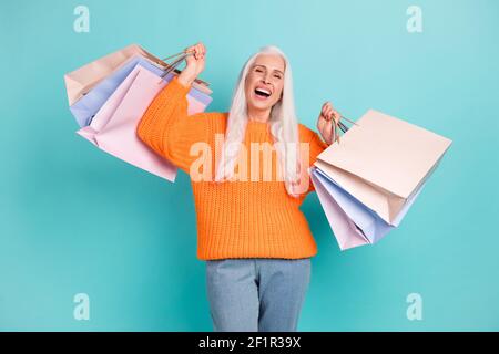 Photo de joyeuse femme âgée excitée soulever des sacs client heureux sourire isolé sur fond bleu pastel Banque D'Images