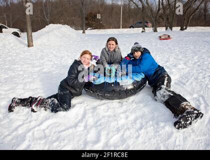 En hiver, les enfants s'entourent d'un tube de neige sur une colline en traîneau. Banque D'Images