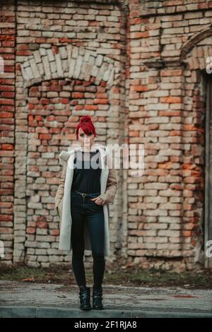 Une photo du corps d'une belle fille souriante aux cheveux rouges avec des bangs portant un manteau d'hiver chaud marron la mettant main sur la poche Banque D'Images