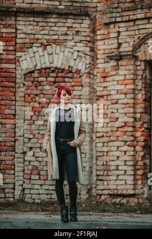 Une photo du corps d'une belle fille souriante aux cheveux rouges avec des bangs portant un manteau d'hiver chaud marron la mettant main sur la poche Banque D'Images