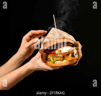 Les mains des femmes tiennent un grand cheeseburger sandwich avec du fromage de boeuf en marbre bacon avec fumée à la vapeur Banque D'Images